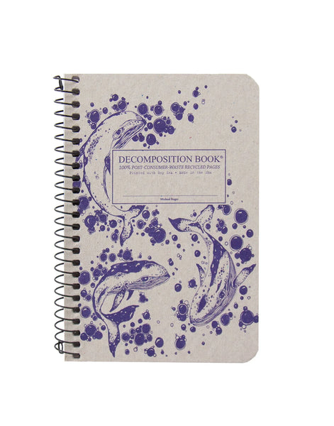 A spiral-bound  pocket sized decomposition book with a beige cover featuring three humpback whales and dark purple ink-blot illustrations. The cover text reads 'DECOMPOSITION BOOK' and '100% POST-CONSUMER-WASTE RECYCLED PAGES'. Printed with Soy Ink. Made in the USA. 