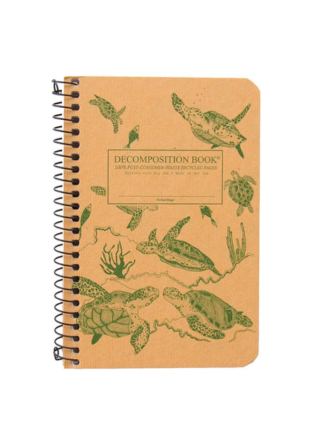 A side spiral-bound decomposition book with a orange cover featuring green sea turtle illustrations and a black wire coil binding. Written in the center, Decomposition Book, 100% post-consumer-waste recycled pages. printed with soy ink, made in usa